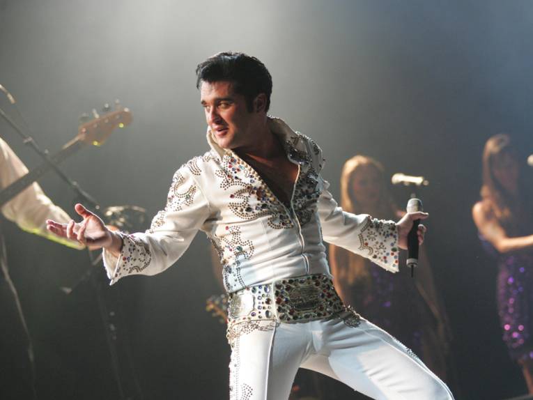 Ein Mann mit weißem Elvis-Kostüm auf der Bühne.