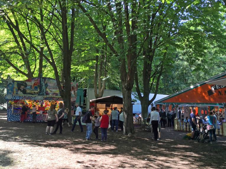 Menschen vor einer Luftballonwurfbude, einem Essensstand und einem Festzelt