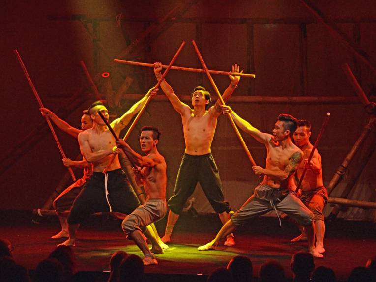 Sechs Männer in kraftvoller Pose mit Bambusstäben