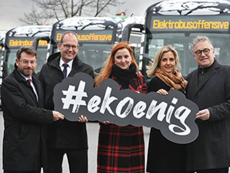 Zwei Frauen und drei Männer halten ein Schild mit der Aufschrift "#ekoenig", im Hintergrund stehen beklebte Busse