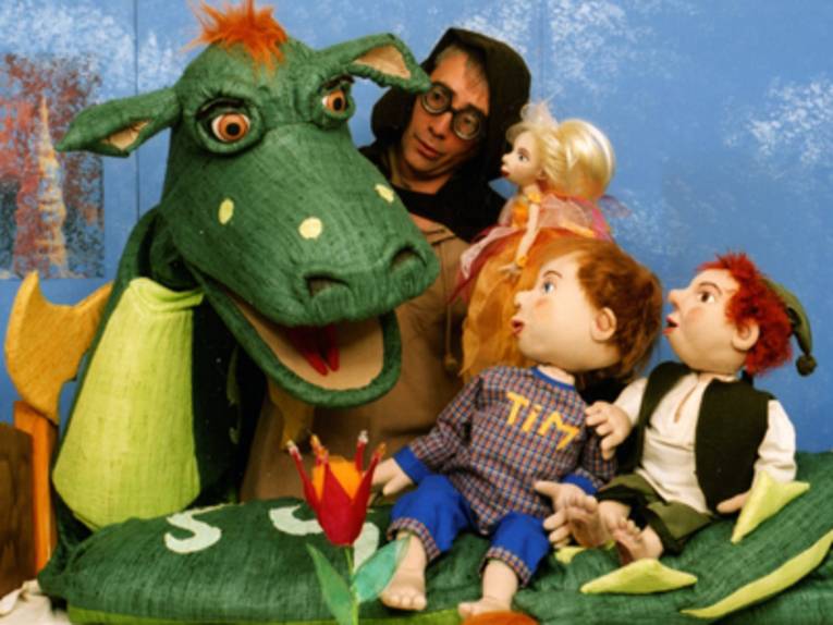 Ein Mann mit einer großen Drachenfigur und drei Puppen