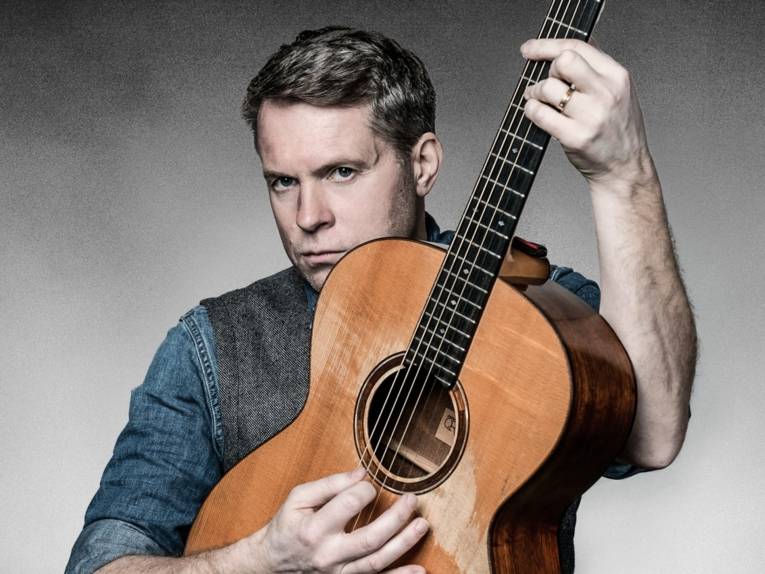 Mann, der eine Gitarre hält und ernst guckt.