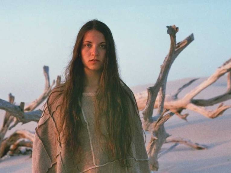 Junge Frau mit sehr langem Haar in einer Wüstenlandschaft mit abgestorbenen Bäumen