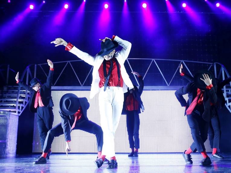 Männer in Schwarz-roten Anzügen auf der Bühne, Ein Michael Jackson-Immitator steht in der Mitte.