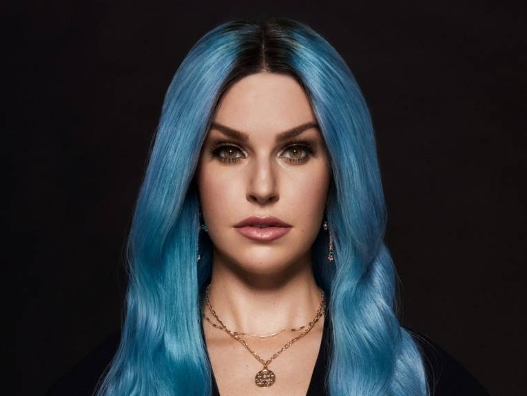 Eine Frau mit blauen Haaren vor einem schwarzen Hintergrund.