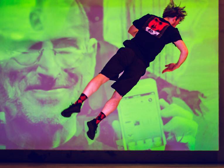 Mann springt vor einer Leinwand auf einer Bühne