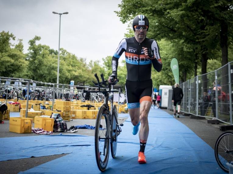 Mann im Sportdress läuft und schiebt dabei ein Rennfahrrad