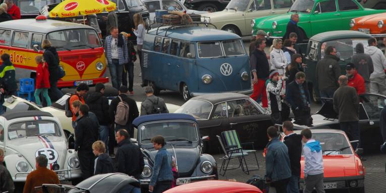 Menschen besichtigen auf einem Parkplatz viele alte VW-Käfer und andere Fahrzeugen