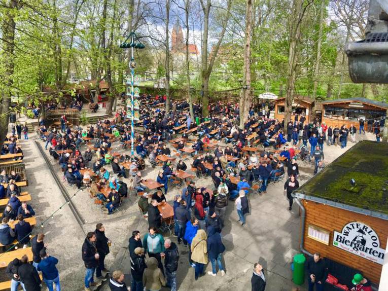 Menschen auf langen Bänken an Tischen im Freien.