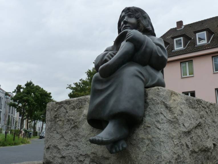 Skulptur eines sitzenden Mädchens, das ein übergroßes Ohr in den Händen hält