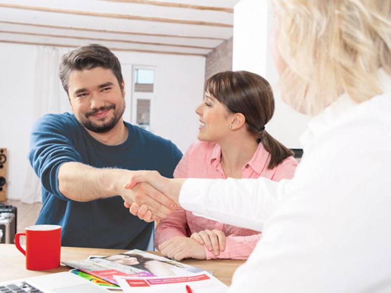 Eine Frau und ein Mann geben sich die Hand, eine weitere Frau sitzt neben dem Mann.