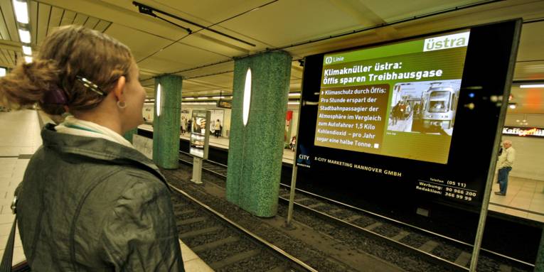 Frau sieht sich eine Nachricht auf einer Leinwand in einer U-Bahnstation an.