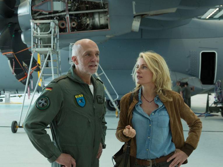 Mann in Bundeswehruniforum und Frau vor einem Transportflugzeug in einer Halle