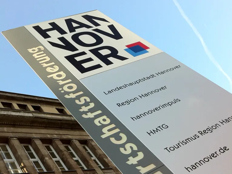 Gebäude, vor dem eine Säule mit Schriftzügen steht
