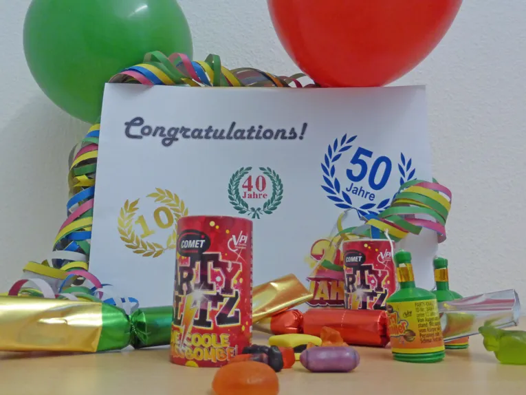 Tischfeuerwerk, Luftschlangen und Luftballons um ein Schild mit Jubiläumszahlen