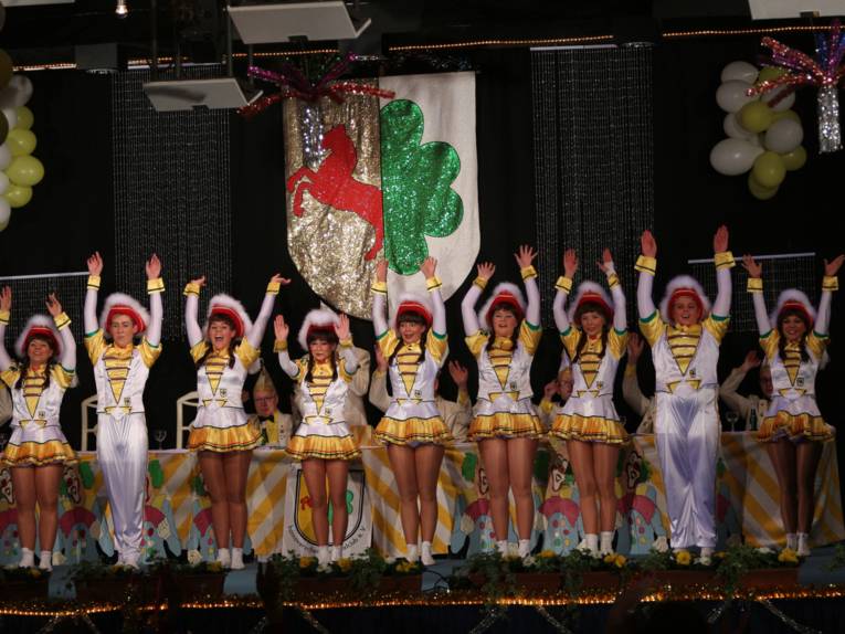 Tanzende Mädchen in Karnevalsuniform auf einer Bühne aufgereiht.