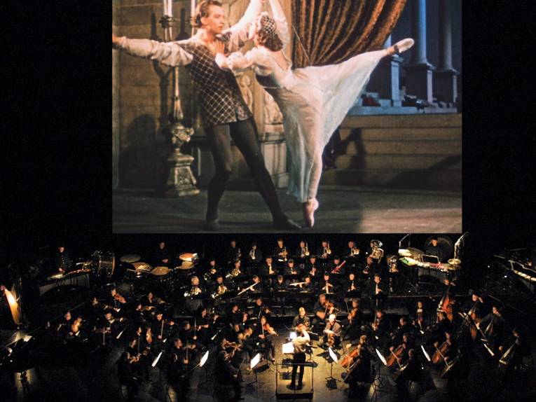 Orchester vor Filmleinwand auf der ein tanzendes Paar zu sehen ist.