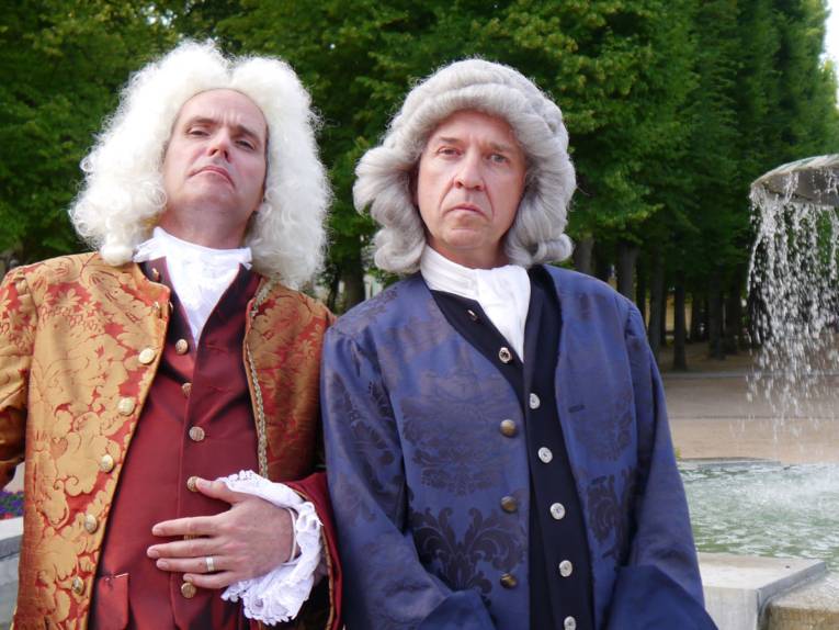 Zwei Männer mit Perücken und Kleidung aus der Barockzeit.