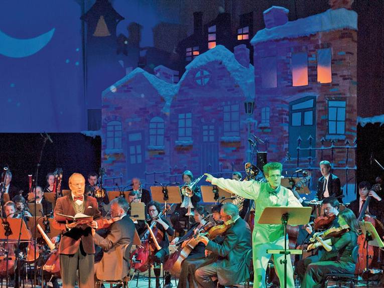 Orchester auf Bühne mit Dirigent und Sänger farbig angestrahlt