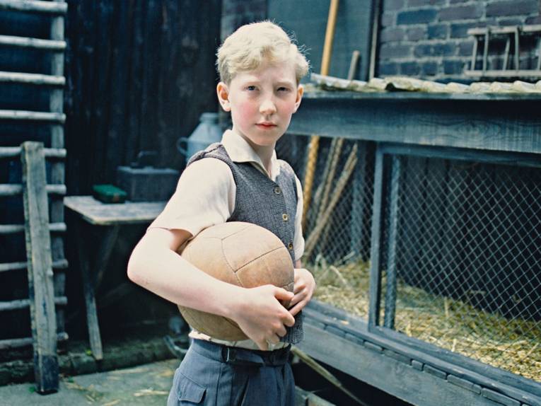Junge mit braunem Lederfußball vor einem Kaninchenstall
