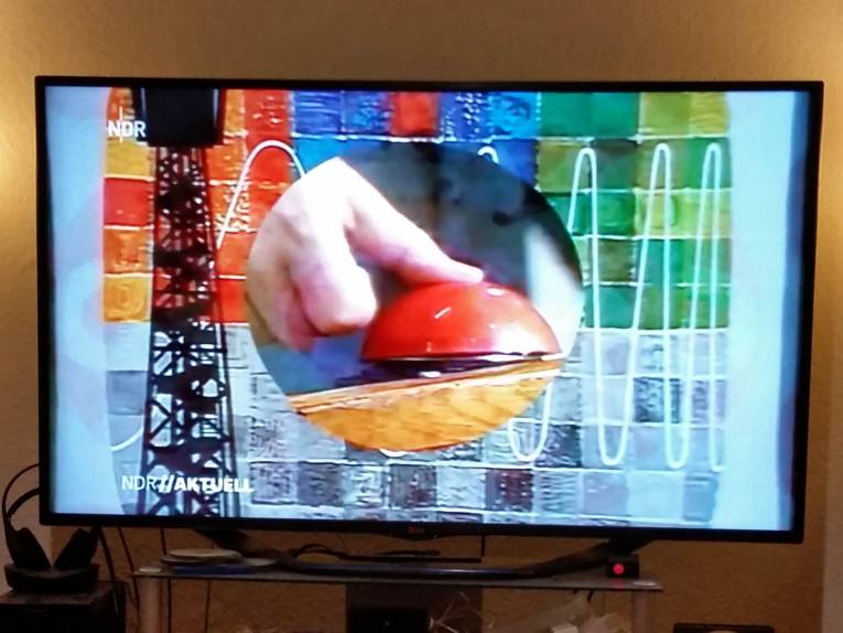 Fernsehbild in Farbe, das einen einen Daumen, der auf einen Knopf drückt, zeigt