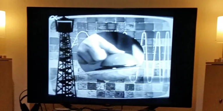 Fernsehbild in Schwarzweiß, das einen einen Daumen, der auf einen Knopf drückt, zeigt