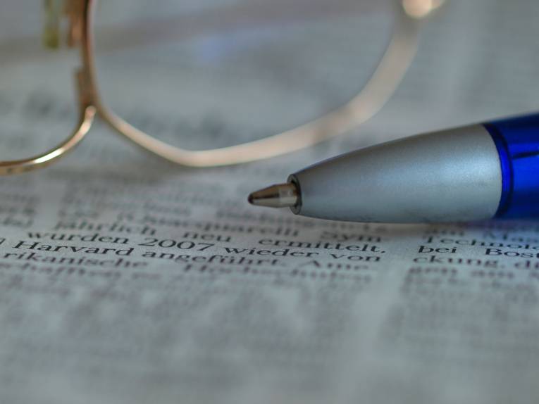 Zeitung, auf der ein Kugelschreiber und eine Brille liegen.