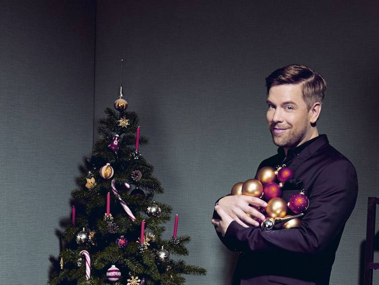 Ein Mann mit Christbaumkugeln in den Händen neben einem Weihnachtsbaum