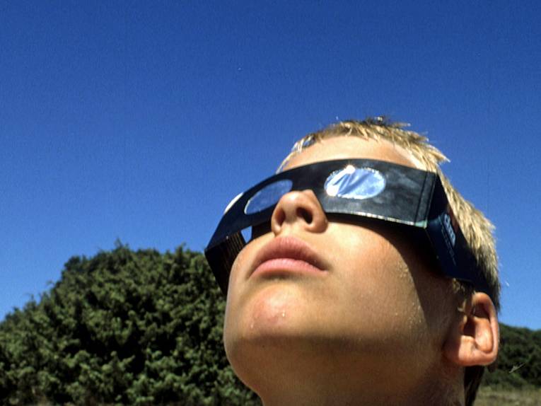 Junge mit Schutzbrille blickt in die Sonne.