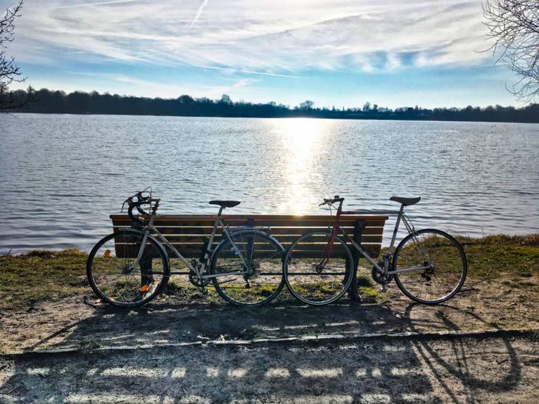 Zwei Fahrräder lehnen an einem See an einer Bank.