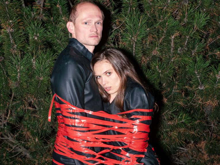 Mann und Frau stehen dicht aneinander, umwickelt mit rotem Band