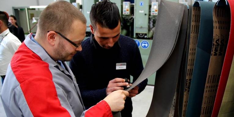Ein junger Mann schaut sich mit einem Ausbilder Schleifpapierbänder an.