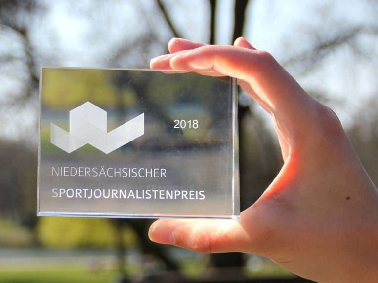 Eine Hand hält ein durchsichtiges Viereck mit der Aufschrift "Niedersächsischer Sportjournalistenpreis 2018"