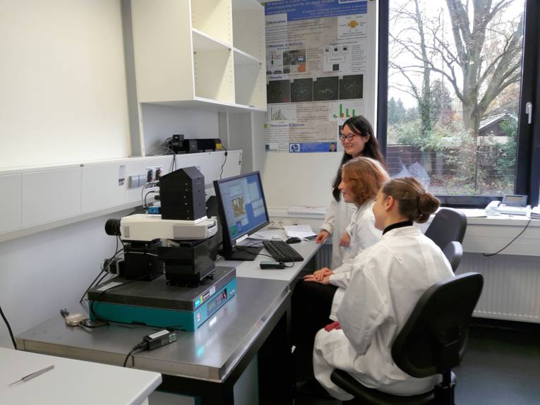 Drei Frauen in weißen Kitteln vor einem Monitor.