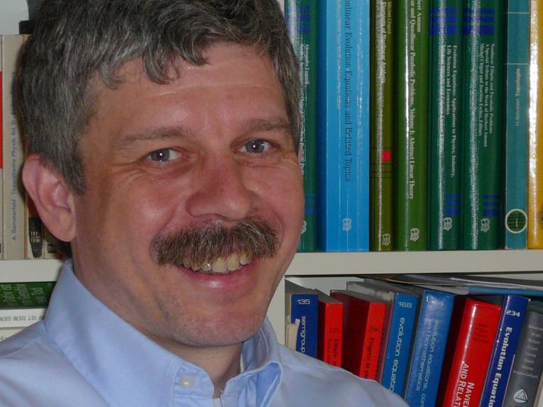 Porträtfoto eines Mannes, im Hintergrund sind Bücher zu sehen.