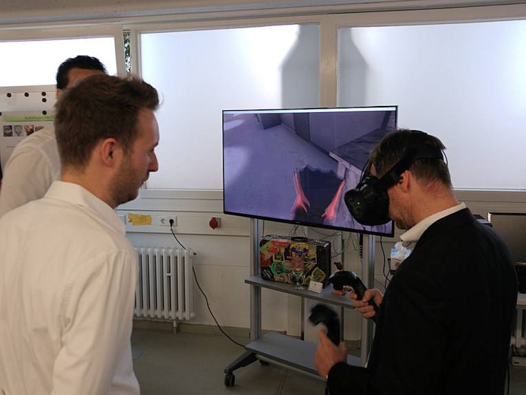 Männer vor Monitor, einer hat eine VR-Brille auf