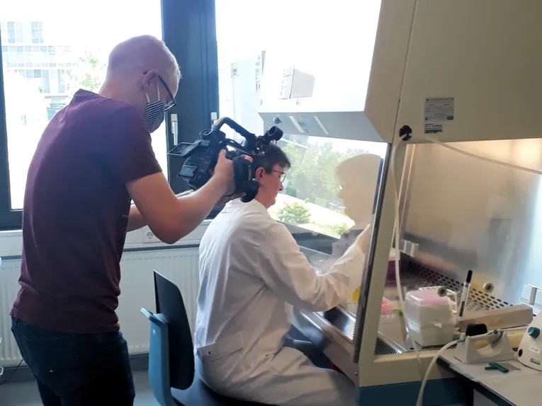 Ein Mann filmt eine Frau in weißem Kittel der Arbeit in einem Labor.