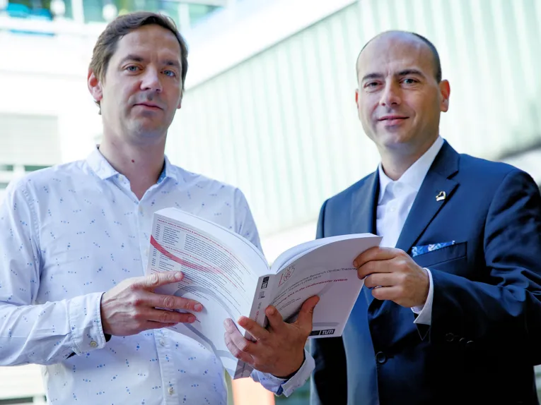 Zwei Männer halten gemeinsam ein aufgeschlagenes Buch 