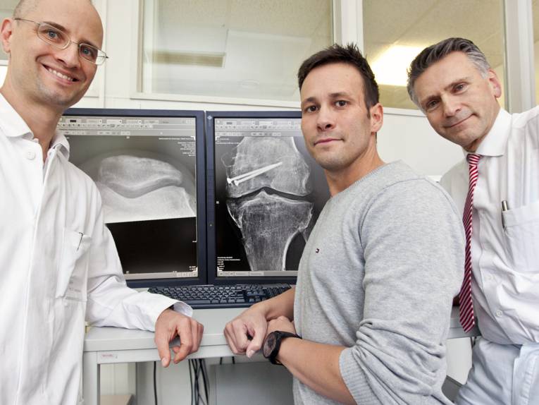 Drei Männer neben einem Bildschirm mit einer Röntgenaufnahme