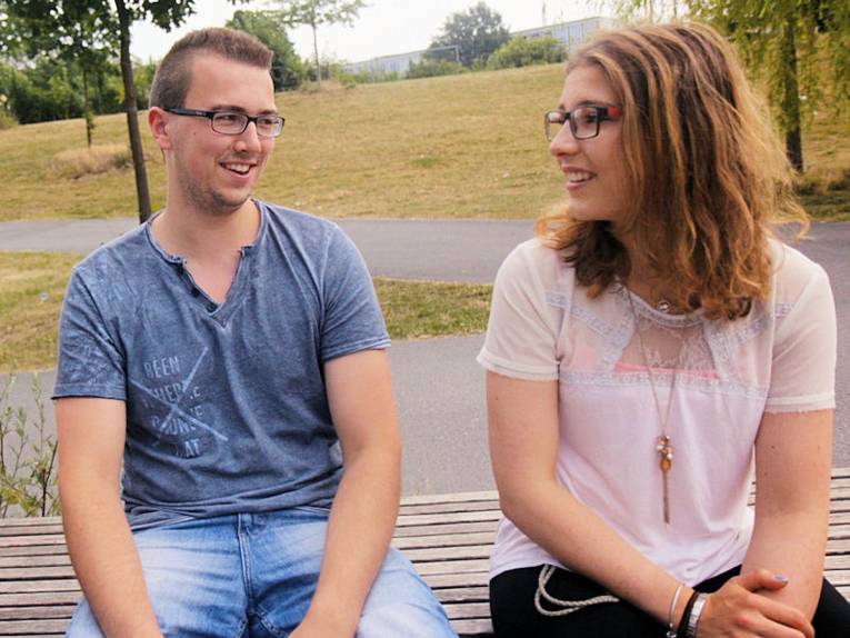 Junge Frau und junger Mann sitzen auf einer Parkbank