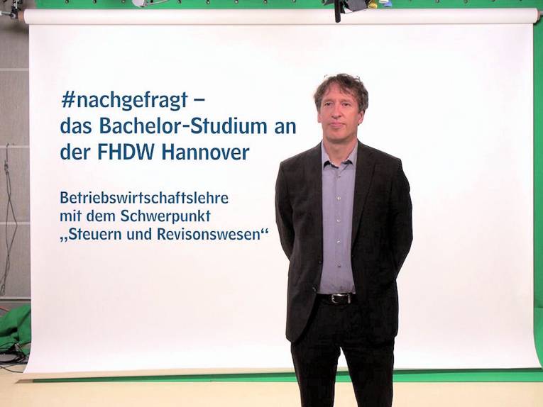 Ein Mann steht vor einer Leinwand mit der Aufschrift: "#nachgefragt - das bachelor-Studium an der FHDW"