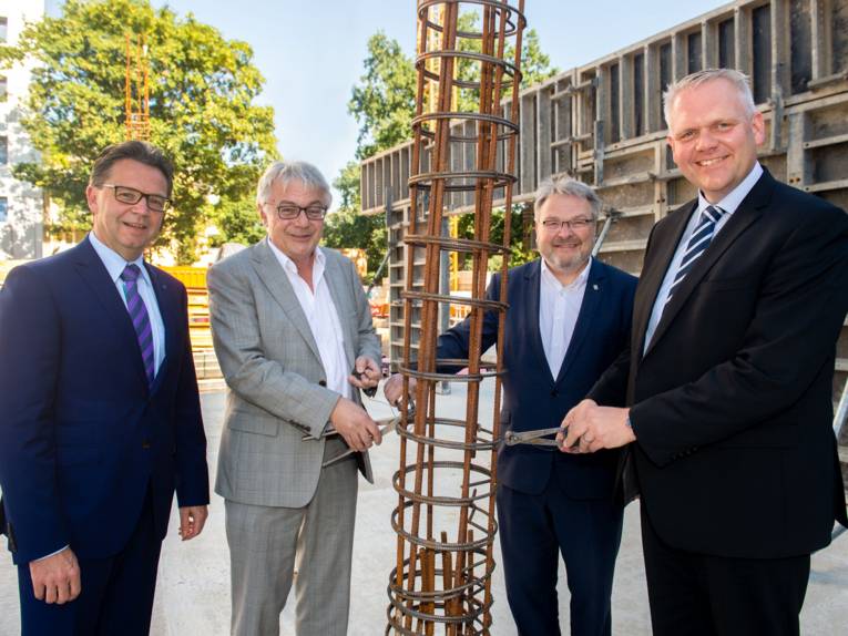 Vier Männer in Anzügen halten eine gerollte Stahlbetonmatte.