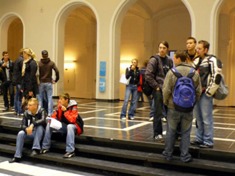 Several students are standing on the stairs in some building.