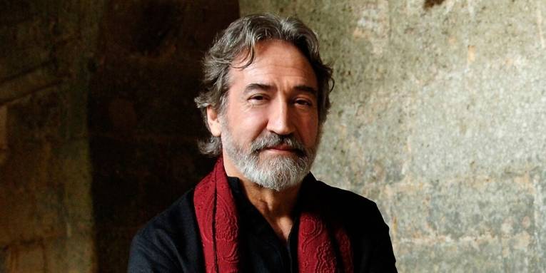 Ein Mann mit grauem Haar und Bart in schwarzem Hemd und rotem Schal.