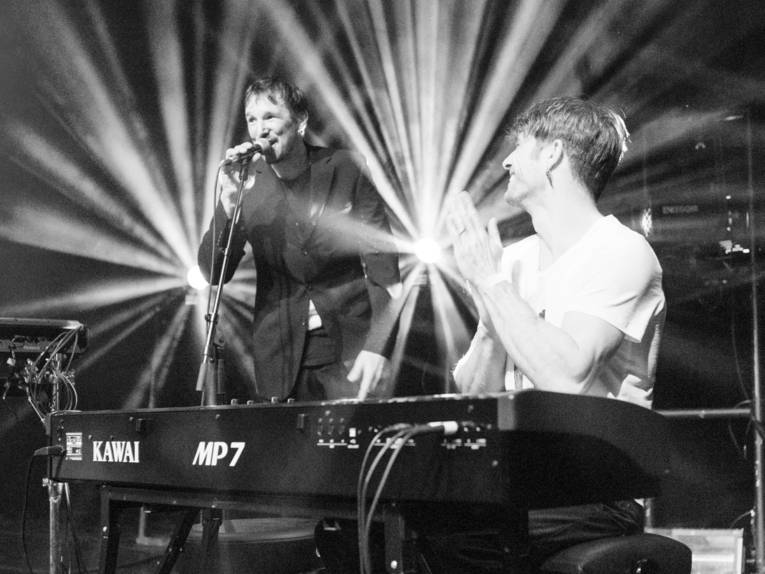 Ein Mann am Klaiver, dahinter ein Mann mit einem Mikrofon