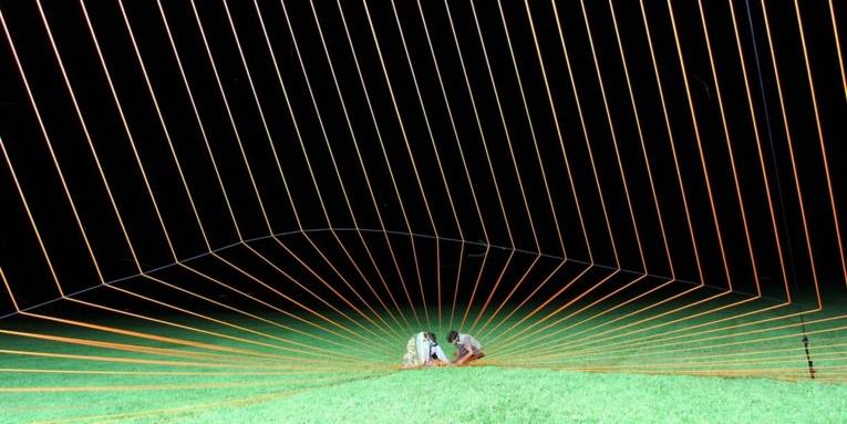 Zwei Personen auf einer Rasenfläche vor einer Art Netz aus grün leuchtenden Seilen.