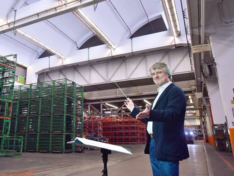 Mann mit Dirigentenstab in großer Fabrikhalle