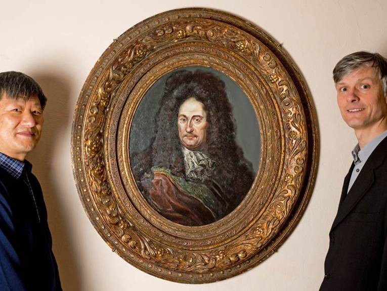 Zwei Männer neben einem historischen Porträt