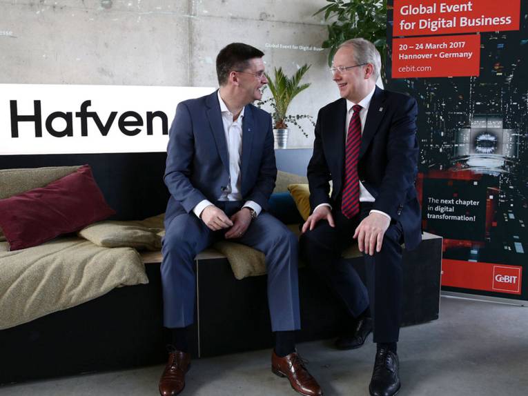 Zwei sitzende Männer in Anzügen blicken sich an.