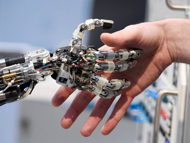 Menschliche Hand und Roboterhand geben sich die Hand.